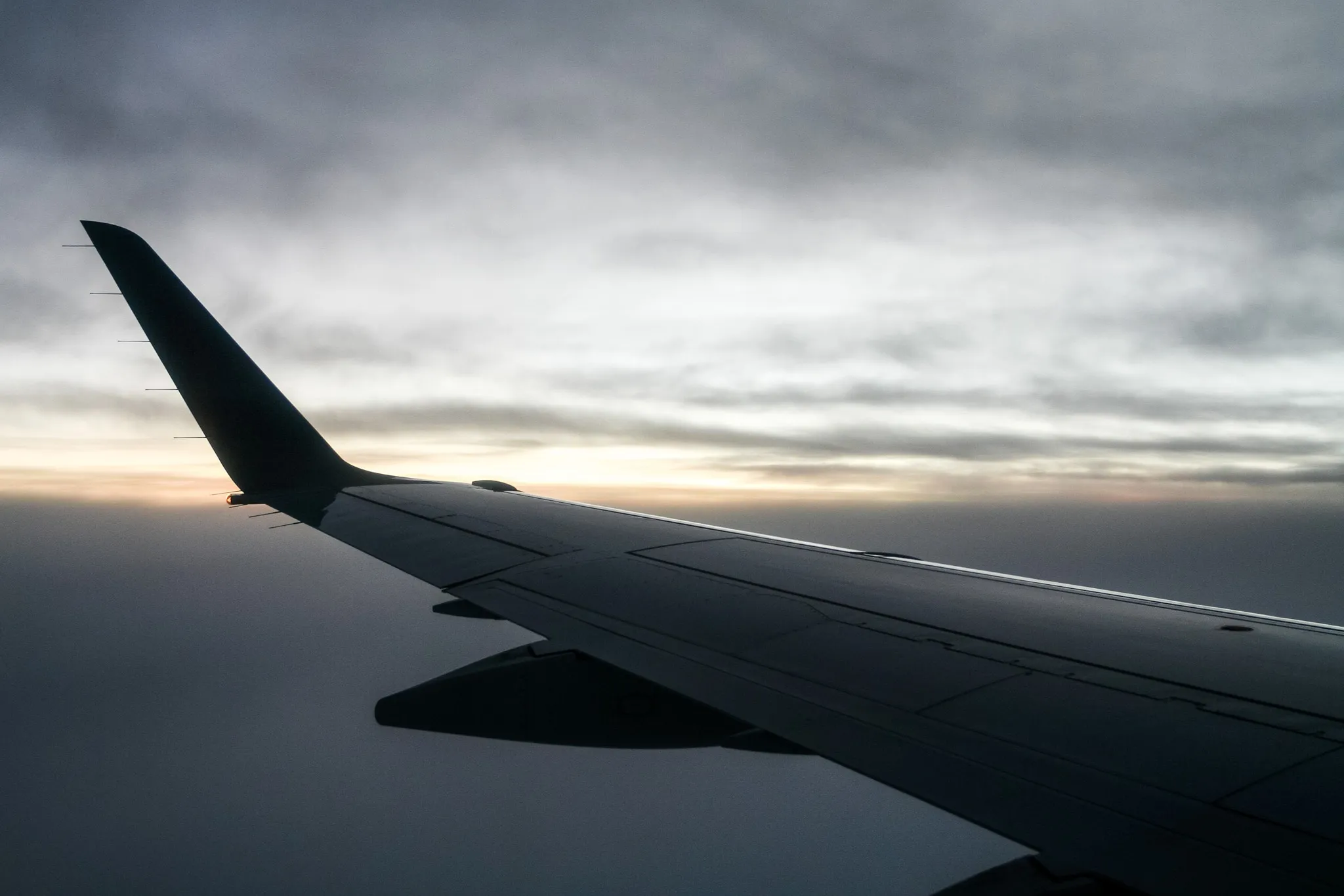 An airplane wing in flight silhouetted against a distant sunrise.